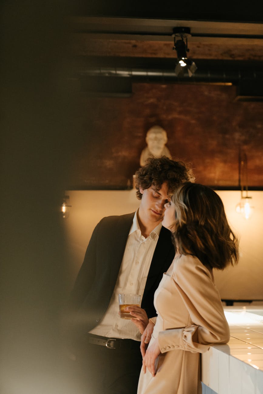 A young couple stands close, sharing a romantic moment at a stylish bar. [pexels]