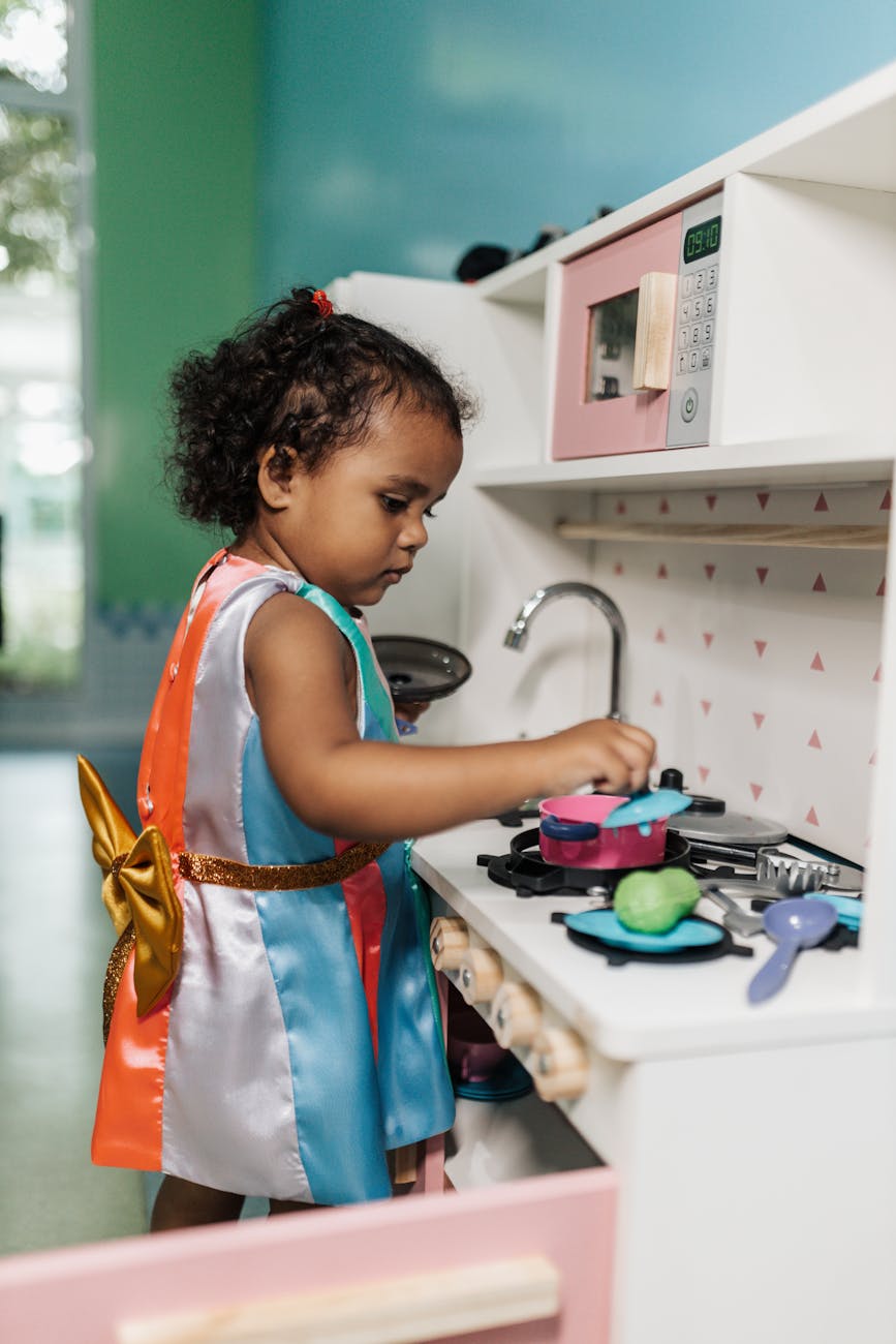 Adorable child focused on pretend play in a toy kitchen indoors. [pexels]