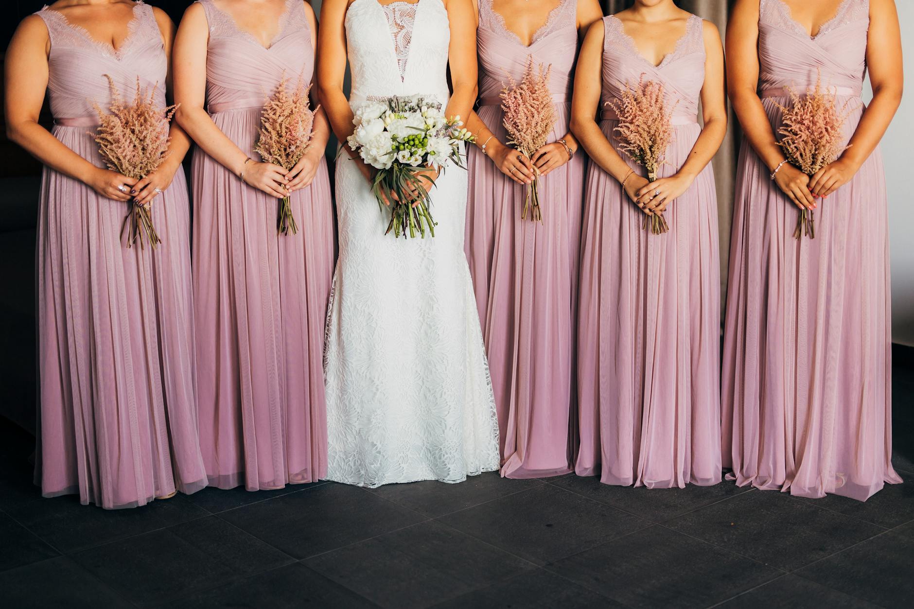 Bride and bridesmaids in elegant attire holding bouquets indoors at a wedding. [pexels]