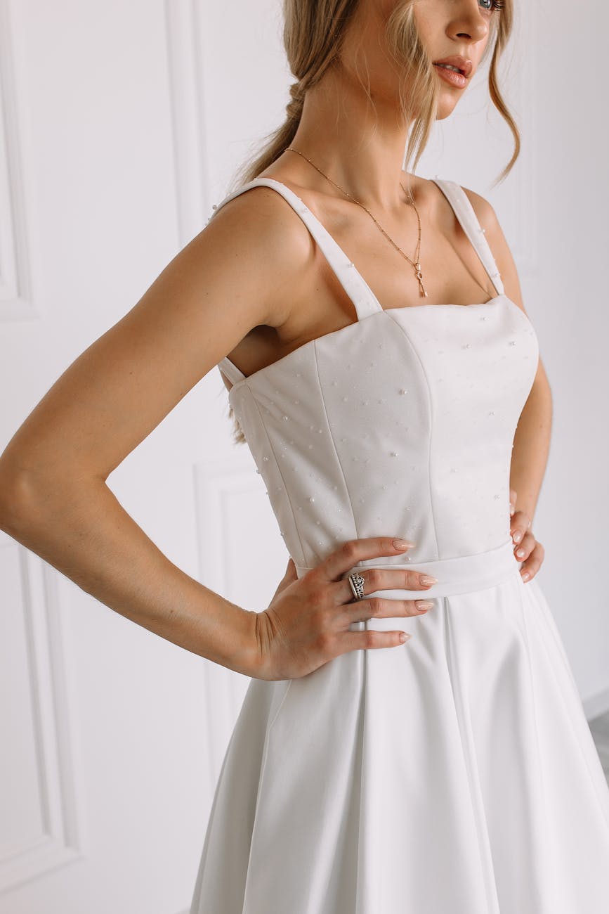 Side view of a woman in an elegant white dress with hands on hips, showcasing the dress details. [pexels]