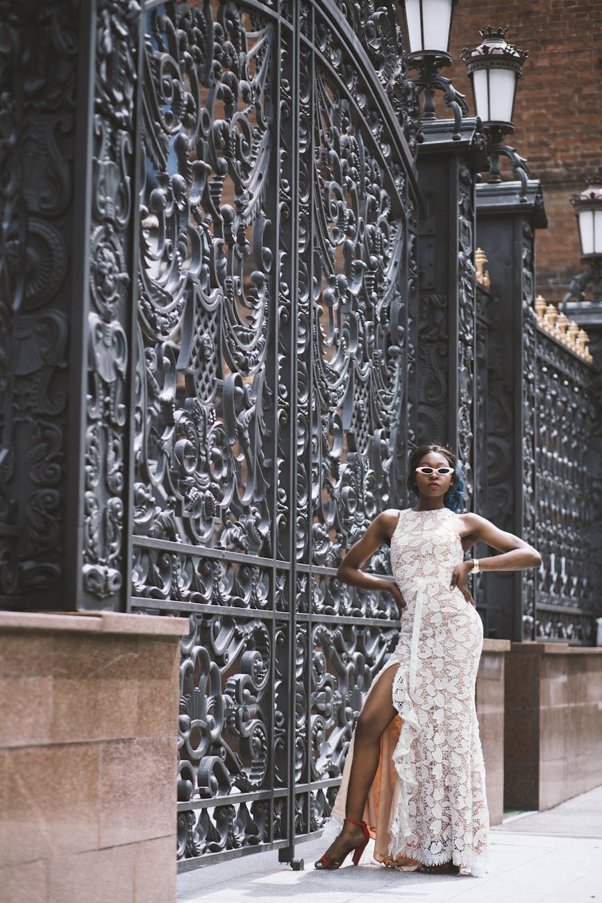 Stylish woman in an evening dress posing by a decorative iron gate outdoors.