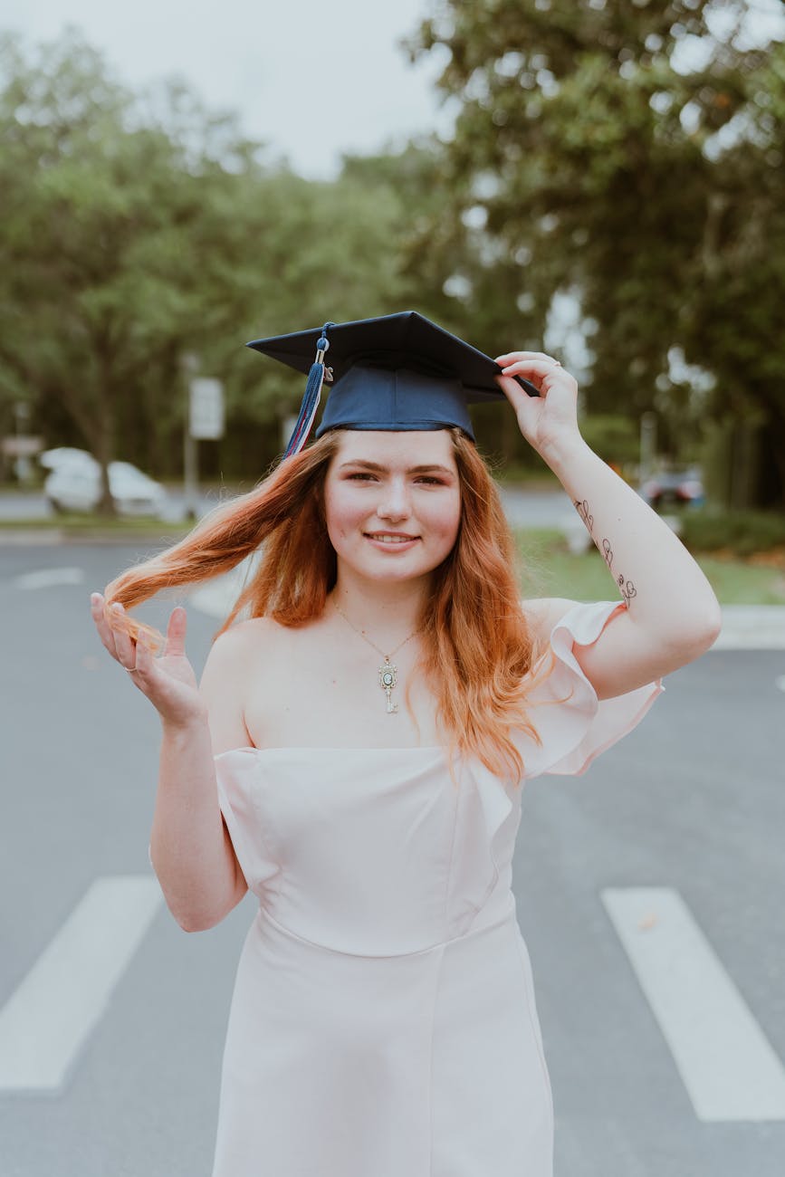 Young woman in a graduation cap and gown celebrating on a sunny day outdoors, exuding happiness and pride. [pexels]