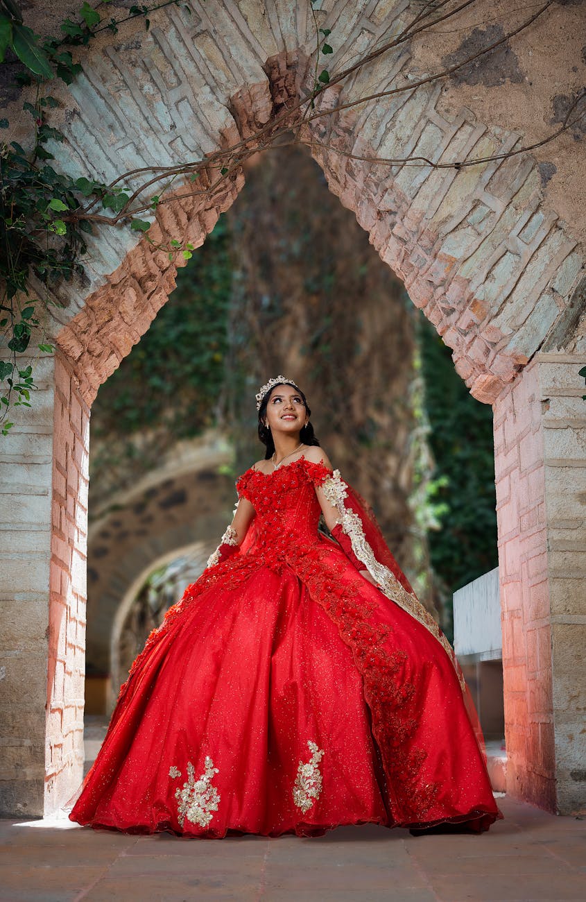 Young woman in red quinceañera dress poses in historic Guanajuato archway, Mexico. [pexels]